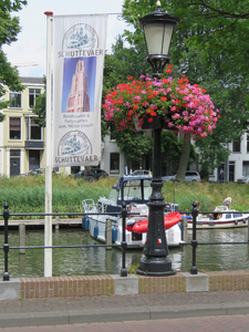 833583 Afbeelding van een banner van Rederij Schuttevaer en van een klassieke straatlantaarn met bakken vol bloeiende ...